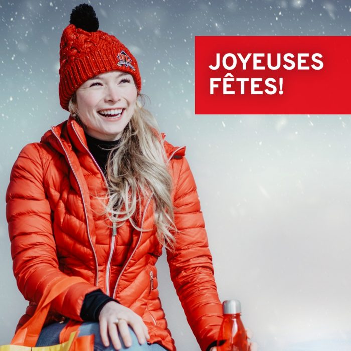 Joyeuses fêtes! Photo d'une jeune étudiante souriante sous la neige. Elle est habillée avec les vêtements de l'Université Laval.